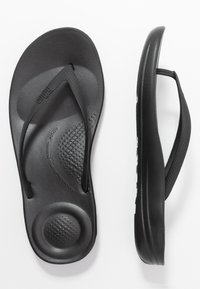 Sandales en caoutchouc noires, dotées de brides texturées et d'une semelle rembourrée avec un motif circulaire en relief.