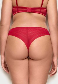 Czerwony siatkowy thong z gładkim wykończeniem, niskim stanem i minimalnym zakryciem z tyłu. Posiada cienki, elastyczny pas, zapewniający pewne dopasowanie.