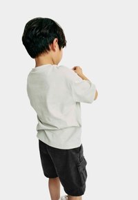 T-shirt en coton gris clair à manches courtes, associé à un bermuda noir cargo de longueur genou avec des poches latérales. Vue arrière d'un enfant.