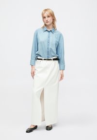 Himmelblaues Jeans-Hemd mit dekorativen blauen Nähten, kombiniert mit einem weißen, hoch taillierten Rock mit Schlitz vorne und schwarzem Gürtel.