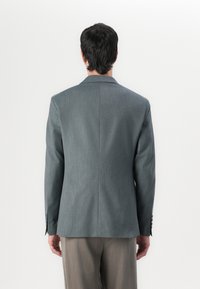 Grå skräddarsydd blazer med en slät textur, utrustad med en enkel slits och två knappar på ärmarna, kombinerad med ljusgrå byxor.