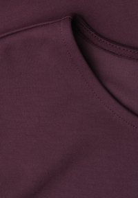 Gros plan sur un tissu bordeaux montrant des coutures détaillées le long d’une couture courbe sur un vêtement.