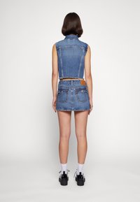 Denim crop topp och mini kjol-set i ljusblått. Kjolen har bakfickor och fransad nederdel. Modellen bär vita strumpor och svarta plattformsskor.