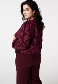 Bordeauxrood jasje met bloemmotief en pofmouwen, met een getextureerd oppervlak, gecombineerd met bijpassende broek; de aansluitende snit benadrukt de taille.