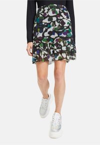 Black mini skirt featuring a layered ruffle design with a colorful abstract pattern in green, purple, and white, paired with white sneakers.