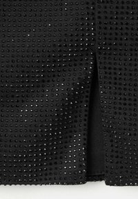 Sort stof med en struktureret overflade, der har hævede prikker og små ædelstene. En slidse detalje er synlig langs den ene side af plagget.