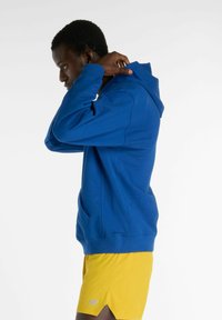 Blå bomullshoodie med en känguruficka och dragsko i huvan, kombinerad med gula shorts. Mjuk textur och avslappnad passform.