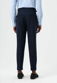 Marineblauwe broek met een getailleerde pasvorm, gladde stof, twee achterzakken en opgerolde zomen, gecombineerd met een lichtblauw shirt met lange mouwen.