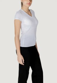 T-shirt bianca a maniche corte con scollatura a V, dal design aderente, realizzata in un leggero tessuto misto cotone, abbinata a pantaloni neri.