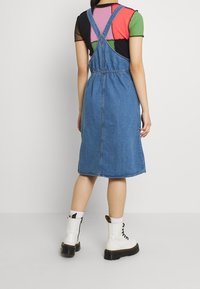 Denim overall klänning med lös passform, medellång, med justerbara axelremmar och åtsnörd midja. Buren med vita snörstövlar.