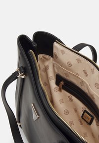 Black handbag with a zip closure, smooth leather exterior, beige patterned lining, multiple interior pockets, and metal hardware accents.