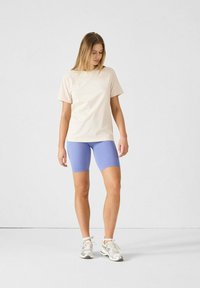 Camiseta beige de manga corta combinada con pantalones cortos de ciclismo azul de canalé y zapatillas de color claro, con un diseño simple y un ajuste modesto.