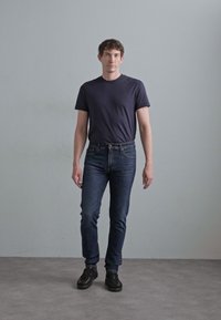 Mornarska majica s crew izrezom, temno modri slim-fit jeans in črni športni copati. Gladek material z udobnim krojem, brez vidnih vzorcev ali logotipov.