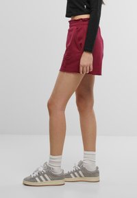 Burgunderfargede bomullsshorts med slitt kant, elastisk midje og sidelommer, kombinert med grå sneakers og hvite ankelsokker.