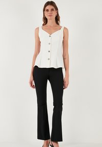 Fehér peplum felső V-kivágással és öt díszes arany gombbal, fekete trapéznadrággal párosítva. Sima anyag és testhezálló kialakítás.