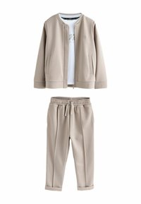 Beige Sportset bestehend aus einer bomberjacke mit Reißverschluss und Mesh-Struktur sowie einem schlichten weißen T-Shirt, kombiniert mit passender, schmal zulaufender Jogginghose.