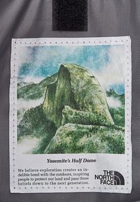 Naszywka tekstylna z ilustracją półkopu Half Dome w Yosemite, otoczona białą przeszywaną krawędzią, z dodatkowymi szczegółami logo marki.