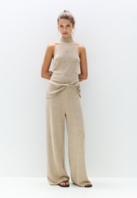 Ensemble coordonné beige tricoté comprenant un haut à col montant et un pantalon large avec un détail froncé à la taille. Texture lisse, coupe décontractée.