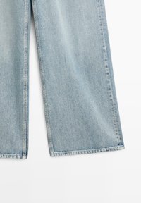 Lichtblauwe jeans met wijde pijpen, zichtbare naden en zomen, plat weergegeven op een witte achtergrond.