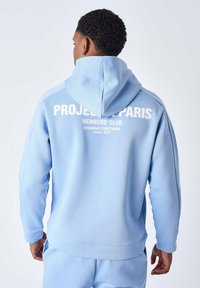Sudadera con capucha de color azul claro, hecha de una tela suave. Presenta texto blanco en la parte posterior: "PROJECT PARIS MEMBERS' CLUB DISEÑANDO STREETWEAR desde 2015."