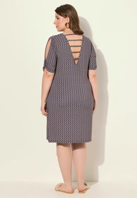 Vestido de estampado navy con mangas cortas, espalda descubierta con tirantes, corte a la altura de la rodilla y tejido suave. Llevado con zapatos beige de tipo slip-on.