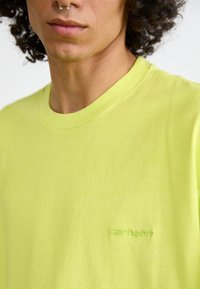 Camiseta de algodón verde lima con cuello redondo y mangas cortas, que presenta un sutil logotipo "Carhartt" en bordado a juego.
