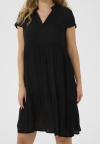 Robe noire à manches courtes, avec un décolleté en V et un col à volants, dotée d'une jupe à volants et d'un tissu léger et texturé.