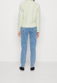 Chaqueta ajustada de color verde claro con mangas largas, combinada con jeans de mezclilla azul. El conjunto se completa con zapatillas negras.