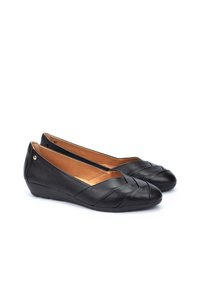 Ballerines en cuir noir avec un design entrecroisé à l'avant et un talon bas. L'intérieur présente une doublure beige chaud et un accent matériel minimal.
