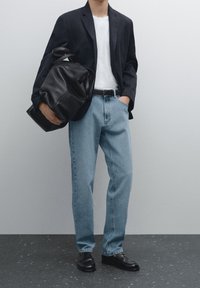 Black blazer, white t-shirt, light blue jeans, and black loafers. Holding a large black leather bag. Smooth fabric and relaxed fit.