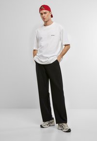 Hvit oversized t-skjorte med svart logo, svarte vide bukser og sølvfargede joggesko. Rød baseballcap fullfører antrekket.