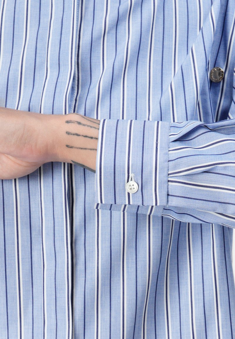 Lichtblauw gestreept shirt met smalle verticale lijnen, knoopmanschetten en een gladde textuur. Opvallende witte en marineblauwe strepen.