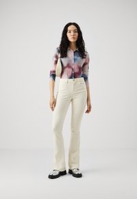 Cămașă lungă din material transparent, tie-dye în nuanțe de albastru, mov și alb; pantaloni cremoși evazați; pantofi cu platformă argintii foarte strălucitori; geantă mică albă.