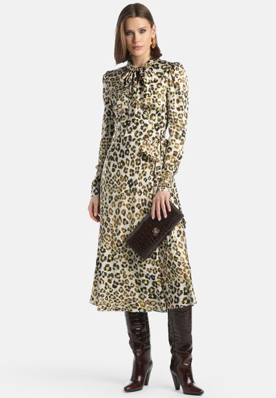 Leopardenmuster Kleid mit einem Schleifen-Ausschnitt, langen Ärmeln und einem fließenden Rock. Kombiniert mit einer braunen Krokodilprägung Clutch und kniehohen Stiefeln.