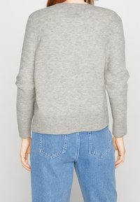 Pull en tricot gris avec un col rond et un ourlet côtelé, associé à un jean en denim bleu clair. Dispose de manches longues et d'une surface texturée.