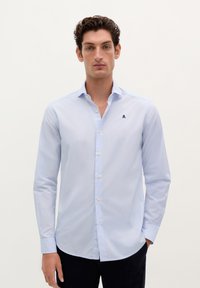 Lichtblauwe langarmshirt met een button-down kraag, witte knopen en een subtiele gestreepte patroon; heeft een klein donkerblauw logo op de borst.