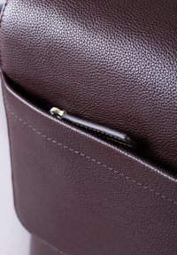 Brown textured leather bag corner featuring a small zippered pocket and visible stitching detail along the edges.