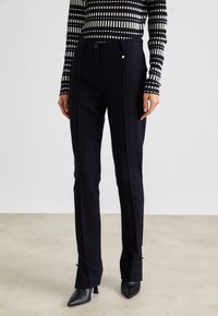 Marineblaue Hosen mit taillierter Passform, hergestellt aus einem glatten Stoff, mit einem einzigen goldenen Akzent und kleinen Schlitzungen am Saum.