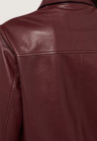 Giacca in pelle bordeaux con texture liscia, colletto a punta e logo "Trussardi" impresso sul retro con dettagli di cucitura visibili.