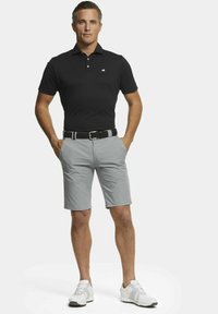 Polo noir avec un design texturé, shorts gris et une ceinture noire. La tenue est complétée par des chaussures de sport blanches.