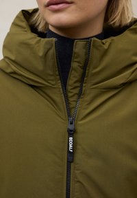 Chaqueta con capucha de color verde oliva, con cuello alto, cierre frontal y herrajes negros; textura suave y diseño minimalista.