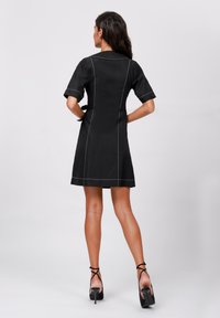 Black dress with short sleeves, white stitching accents, fitted design, and a flared hem. Paired with black strappy high heels.