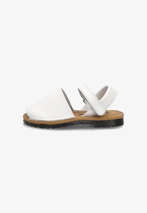 Sandalia de piel blanca con puntera abierta, plantilla marrón clara, suela de goma negra y correa ajustable en el tobillo con cierre de velcro.