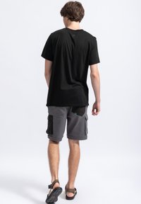 Zwart katoenen T-shirt en grijze cargoshorts met zakaccenten. Sandalen met verstelbare banden maken de outfit compleet. Focus op comfort en functionaliteit.