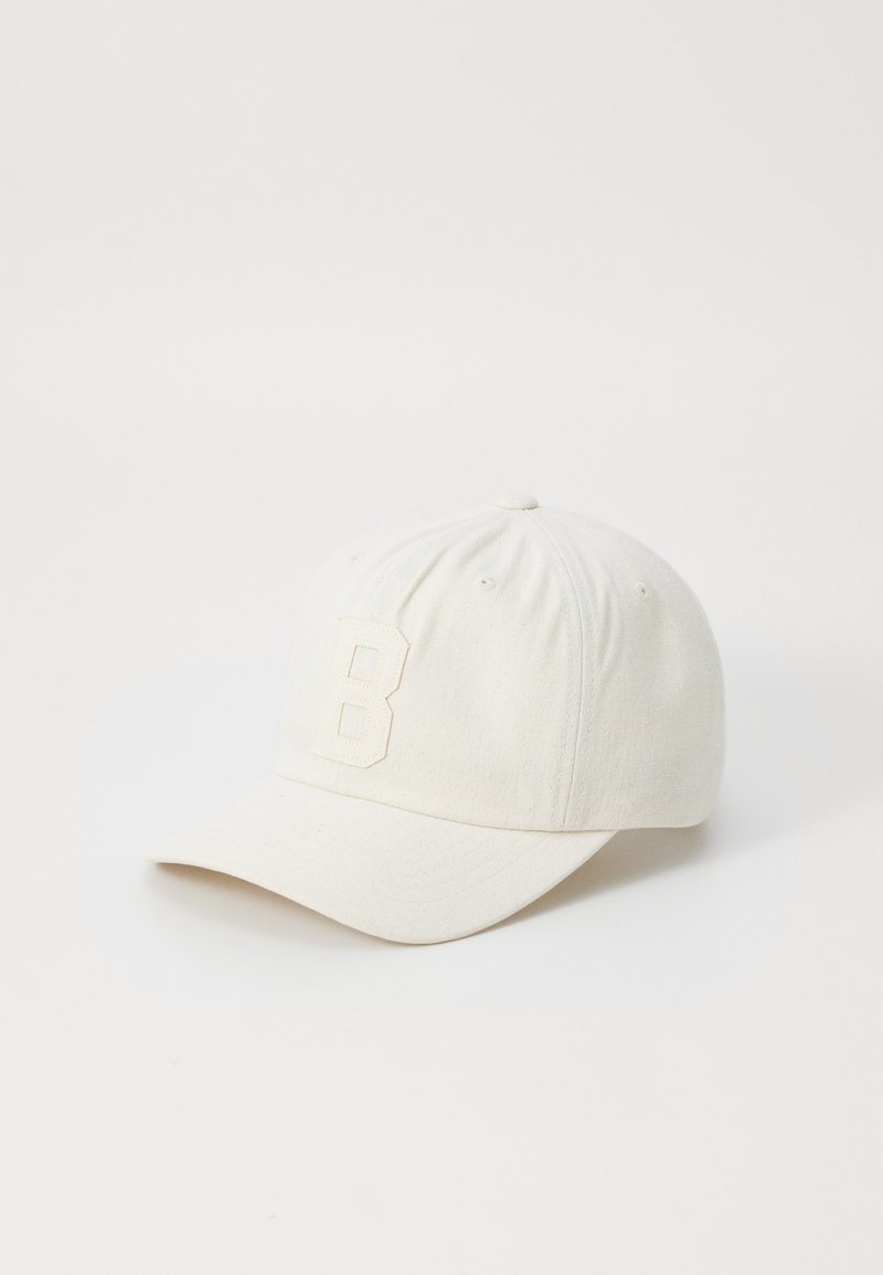 White baseball cap made of textured fabric, featuring a raised "B" emblem on the front and a curved brim.