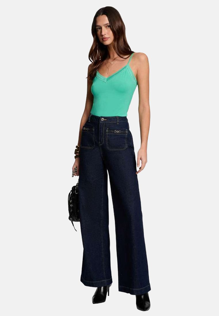 Body vert ajusté avec un décolleté en V, associé à un jean bleu foncé taille haute à jambes larges et des bottes à talons noires, ainsi qu'un sac à main noir.