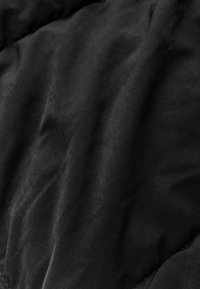 Tissu matelassé noir avec une texture lisse et un léger éclat, affichant un motif de surface froissée et des bords doucement arrondis.