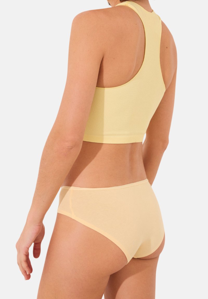 Reggiseno sportivo giallo a coste e slip coordinati, con un design aderente e tessuto liscio, visti dal retro.