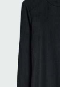 Haut noir à manches longues en maille côtelée avec un col rond haut, présenté sur un fond gris clair.