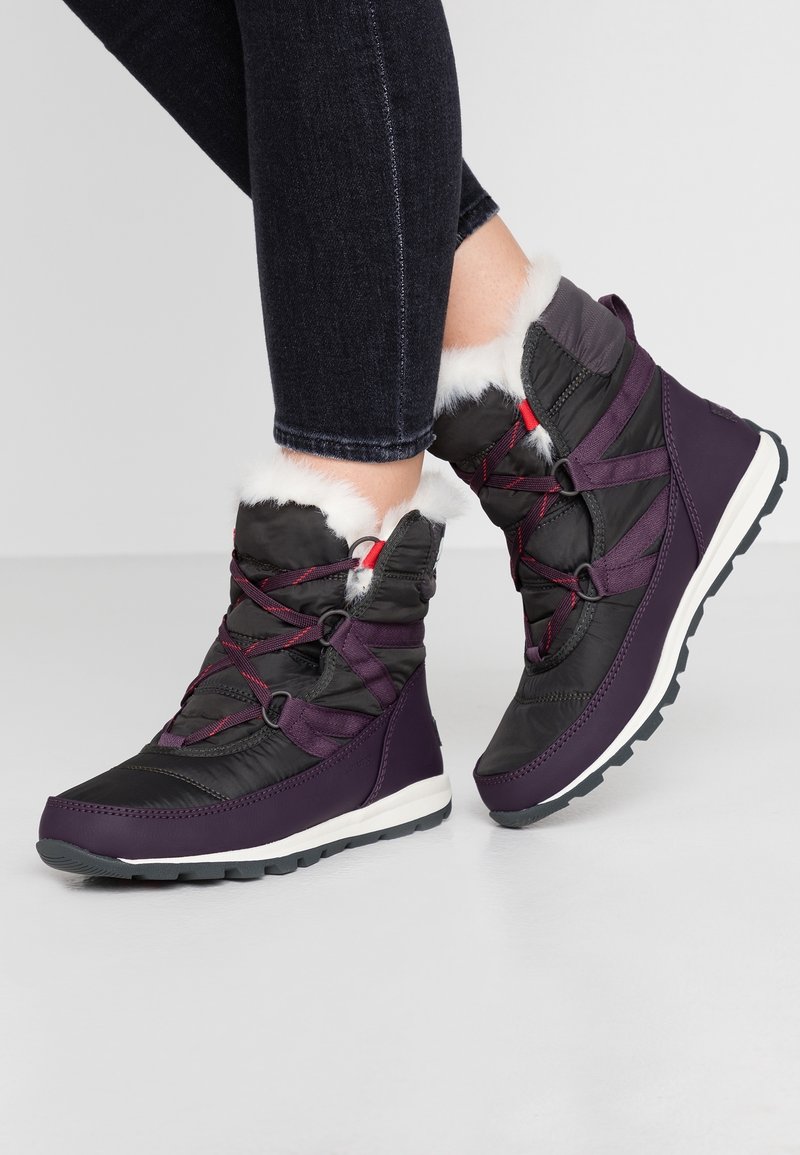 Lila und schwarze isolierte Stiefel mit Kunstfellfutter, ausgestattet mit einer strukturierten Oberfläche, einem Schnürsystem und einer weißen Zwischensohle auf einer gummierten Außensohle.